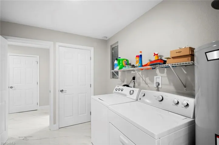 Laundry room with water heater, washing machine and dryer, and light marble finish flooring
