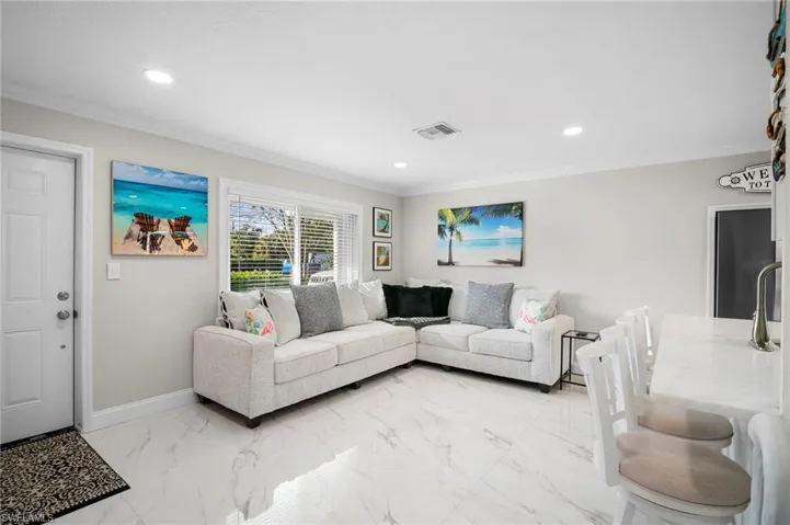 Living room with ornamental molding, light marble finish flooring, and recessed lighting