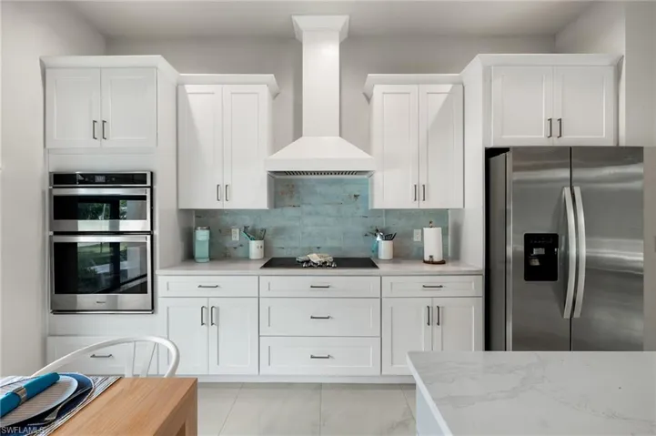 Kitchen featuring appliances with stainless steel finishes, tasteful backsplash, white cabinetry, light stone counters, and wall chimney range hood