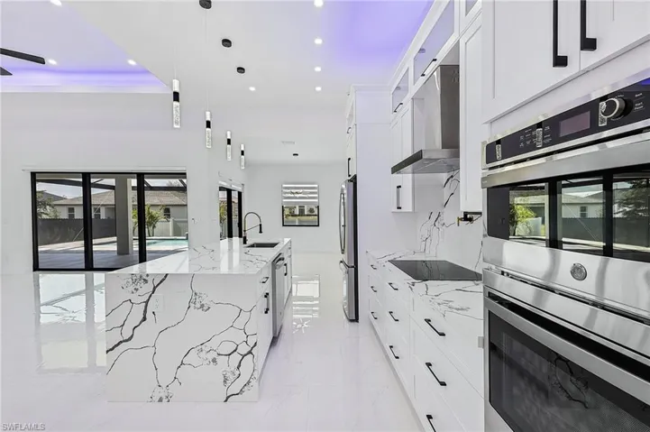 Kitchen featuring a sink, white cabinets, appliances with stainless steel finishes, wall chimney exhaust hood, and marble finish floor
