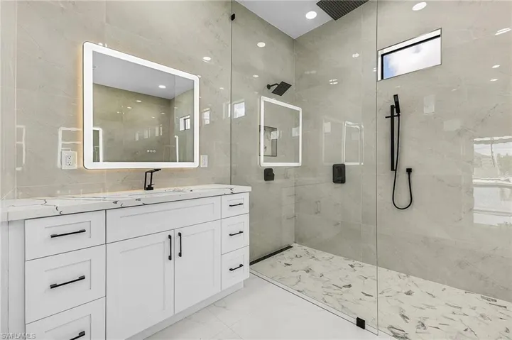 Bathroom featuring tile walls, marble finish floor, vanity, and a tile shower