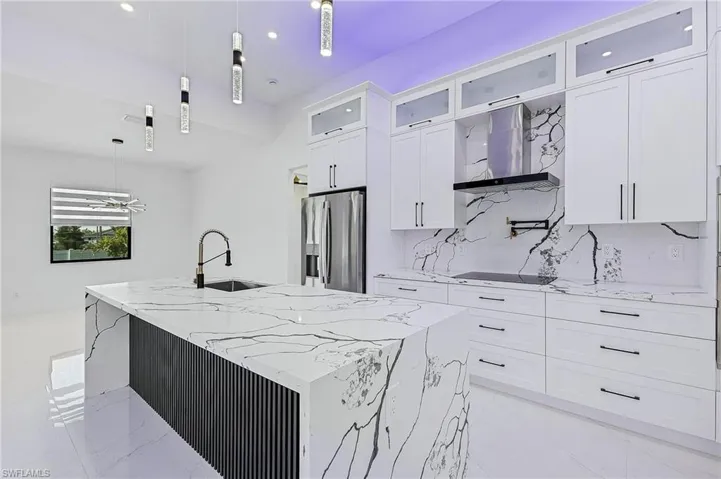 Kitchen with marble finish floor, a center island with sink, a sink, stainless steel fridge, and wall chimney exhaust hood