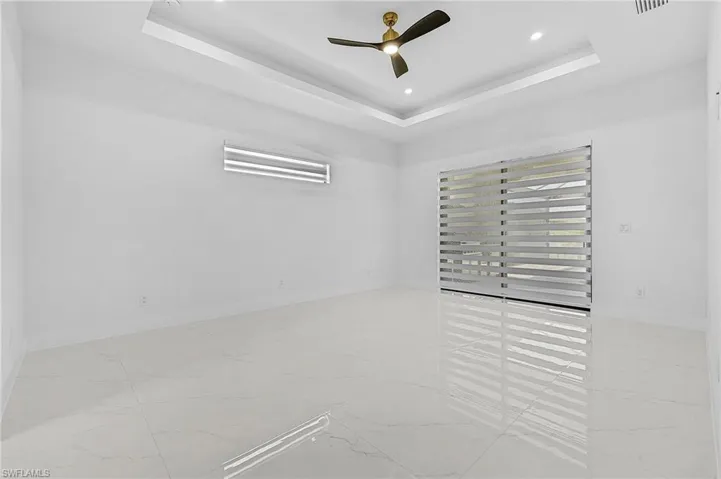 Unfurnished room featuring baseboards, a tray ceiling, recessed lighting, marble finish floor, and a ceiling fan