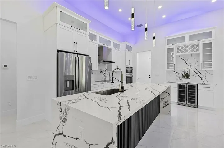Kitchen featuring marble finish floor, beverage cooler, a sink, stainless steel appliances, and white cabinets