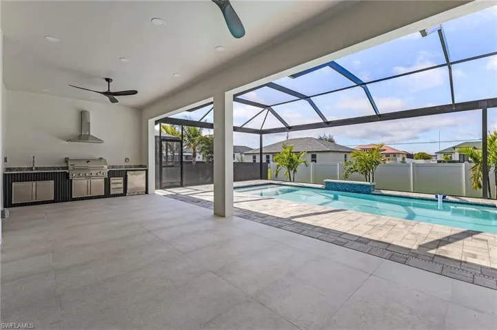 View of swimming pool featuring a summer kitchen with grill, a sink, a mini fridge, lanai with screen enclosure