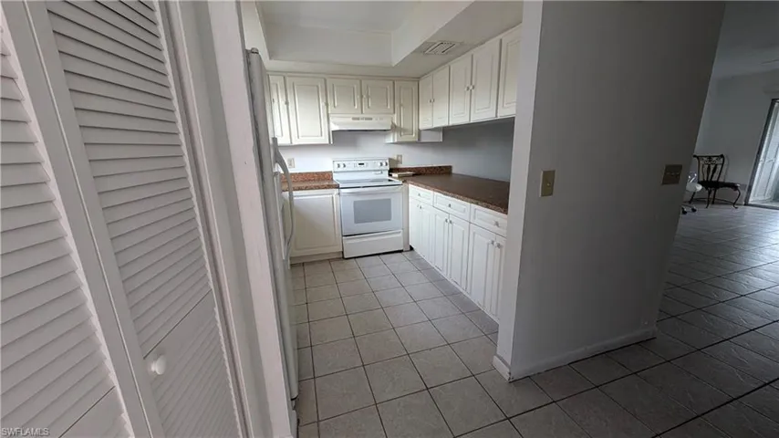 Kitchen with white electric stove, white cabinetry, dark countertops, light tile patterned floors, and freestanding refrigerator