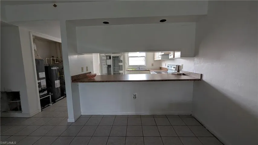 Kitchen with electric stove, light tile patterned floors, electric water heater, dark countertops, and white cabinets