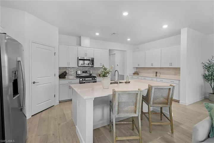 Kitchen with an island with sink, stainless steel appliances, backsplash, and light wood-type flooring