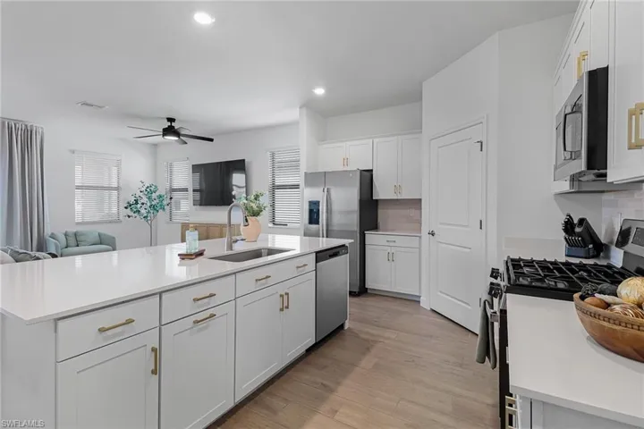 Kitchen featuring stainless steel appliances, a center island with sink, ceiling fan, tasteful backsplash, and sink