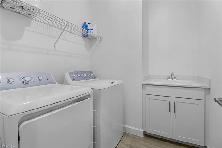 Laundry area with sink, separate washer and dryer, light wood-type flooring, and cabinets