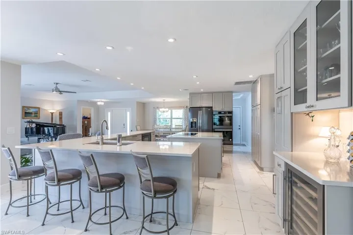 Kitchen featuring gray cabinets, a large island, wine cooler, stainless steel fridge with ice dispenser, and sink
