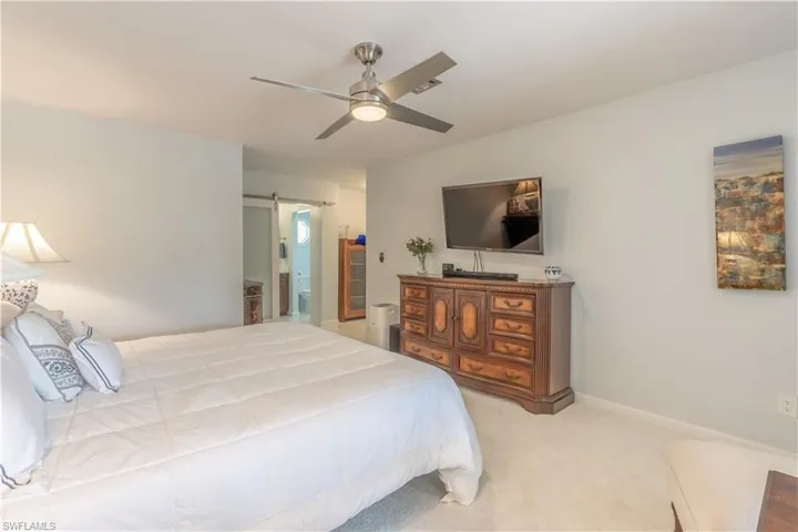 Bedroom featuring light carpet, ceiling fan, and a barn door