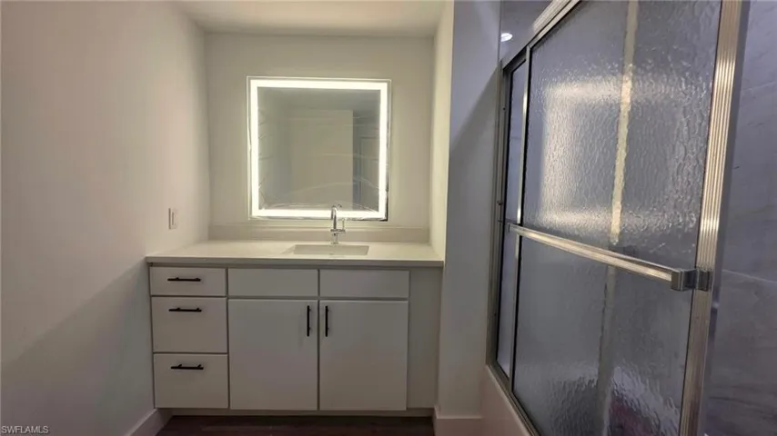 Bathroom featuring vanity, dark wood-style floors, and combined bath / shower with glass door