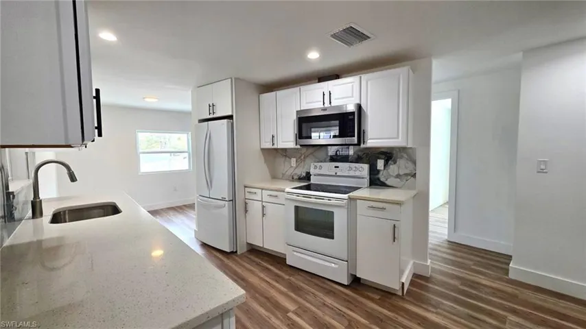 Kitchen with white appliances, white cabinets, dark wood finished floors, light stone countertops, and recessed lighting