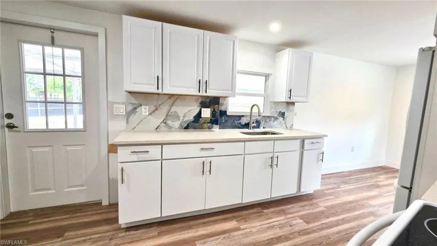 Kitchen with white cabinets, backsplash, light wood-style floors, and freestanding refrigerator