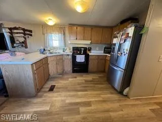 Kitchen with black range, stainless steel fridge with ice dispenser, light countertops, and light wood-style floors
