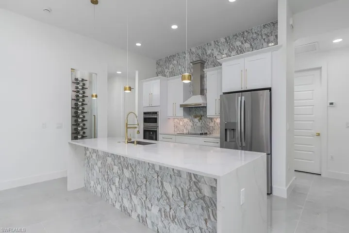 Kitchen featuring wall chimney exhaust hood, appliances with stainless steel finishes, a center island with sink, and pendant lighting
