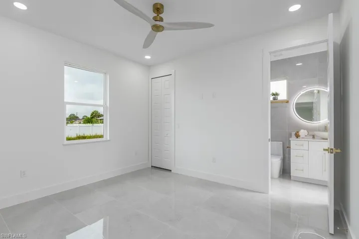 Unfurnished bedroom with ensuite bathroom, ceiling fan, and a closet