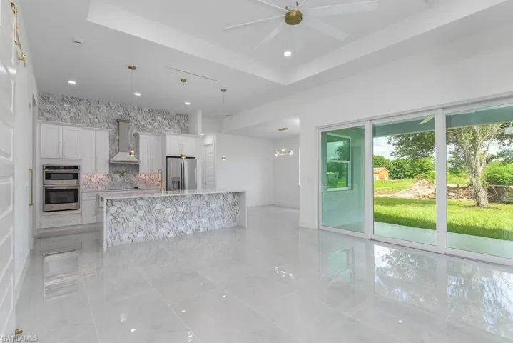Kitchen featuring decorative light fixtures, ceiling fan, appliances with stainless steel finishes, white cabinets, and wall chimney range hood