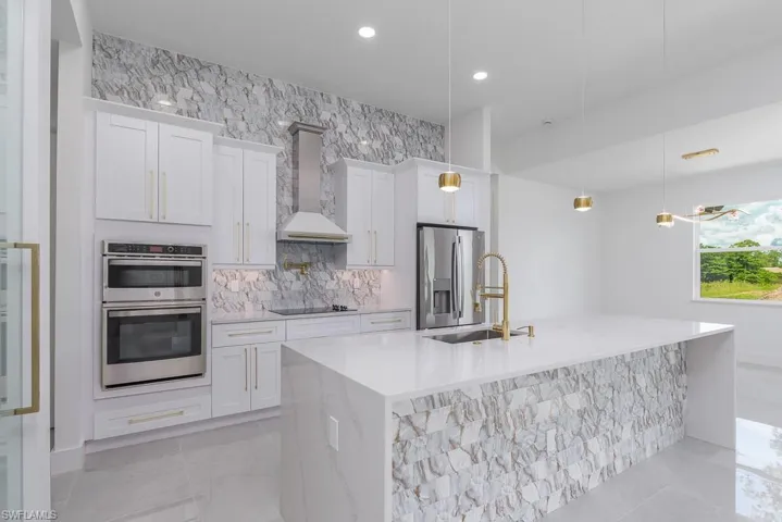 Kitchen with pendant lighting, stainless steel appliances, an island with sink, sink, and wall chimney exhaust hood