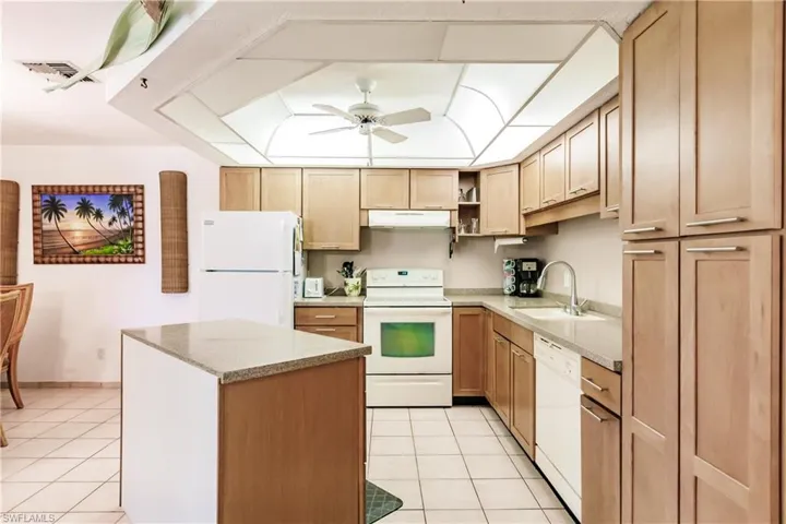 Kitchen featuring a center island, white appliances, sink, light tile flooring, and ceiling fan