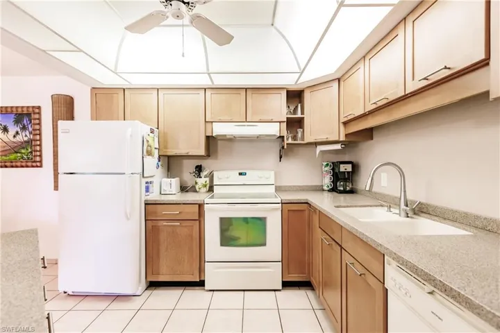 Kitchen with ceiling fan, sink, white appliances, and light tile floors