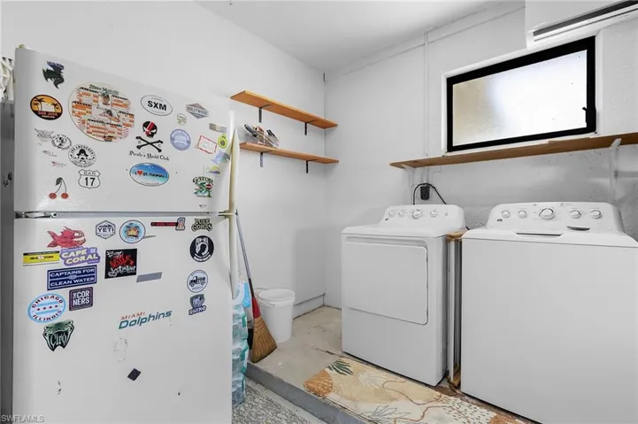 Laundry area in garage, includes refrigerator, washer and dryer, min-split AC/Dehumidifier system, door to side yard, hurricane rated garage door, painted floors, and overhead lighting, shelving for storage