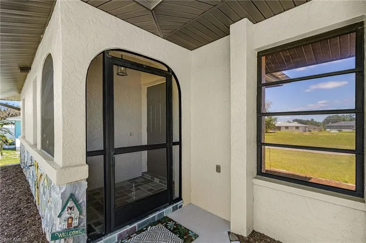 The property features an inviting entrance with a screened porch, stucco exterior, and a decorative stone-clad wall