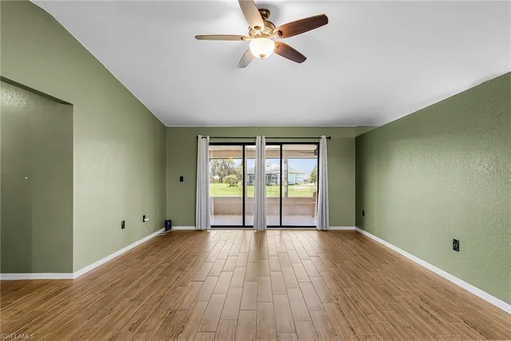 The living area features wood plank style tile flooring, sliding doors to lanai, newer ceiling fan
