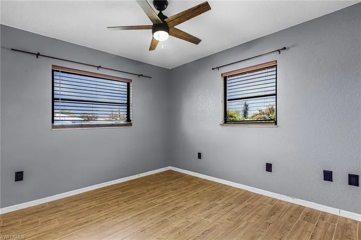 guest bedroom, wood plank style tile flooring, gray walls, and two windows with horizontal blinds