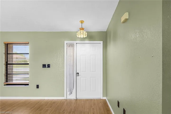 Entryway featuring light green walls, a white door with a side window and sheer curtain, and warm-toned flooring