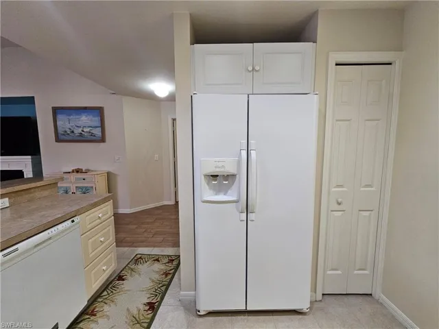Kitchen area featuring a side-by-side refrigerator, upper white cabinetry, light-toned countertops, and tile flooring
