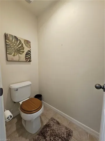 Bathroom featuring a toilet with a wood-finish seat and ceramic tile flooring