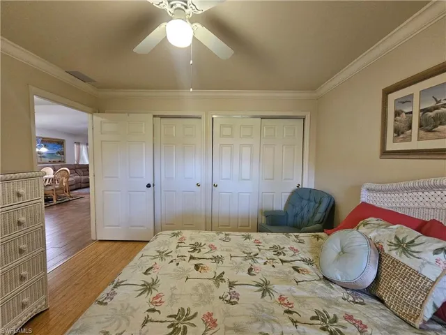 Sleeping area featuring crown molding, a ceiling fan with integrated lighting, and wood-finish flooring