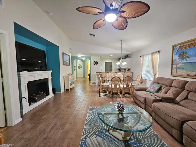 Spacious open-concept living area featuring wood-finish flooring, a vaulted ceiling, and a fireplace with a white mantel
