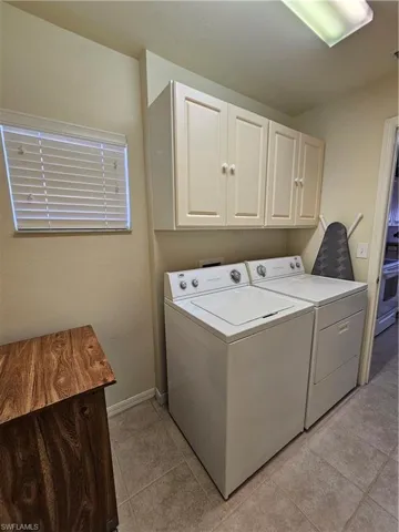 Dedicated laundry area featuring overhead cabinetry, a window with blinds, and tiled flooring