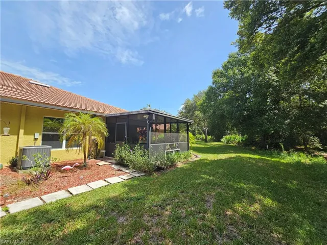 Spacious rear yard with a screened patio, expansive lawn, mature trees, and a terracotta tile roof