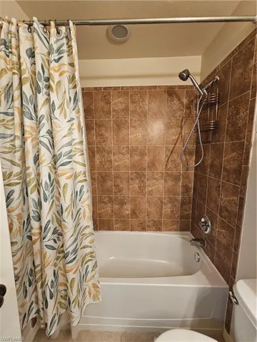 Bathtub and shower combination featuring brown square wall tiles, a ceiling-mounted exhaust fan, and chrome fixtures