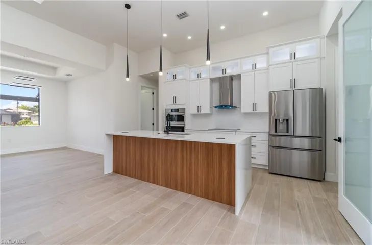 Kitchen with appliances with stainless steel finishes, a center island with sink, white cabinetry, and wall chimney exhaust hood