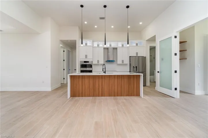 Kitchen with white cabinetry, wall chimney range hood, a center island with sink, light hardwood / wood-style floors, and stainless steel appliances