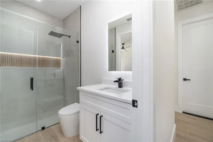 Bathroom with an enclosed shower, vanity, toilet, and ceiling fan