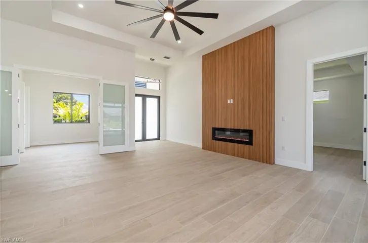 Unfurnished living room with ceiling fan, light wood-type flooring, a fireplace, and a raised ceiling