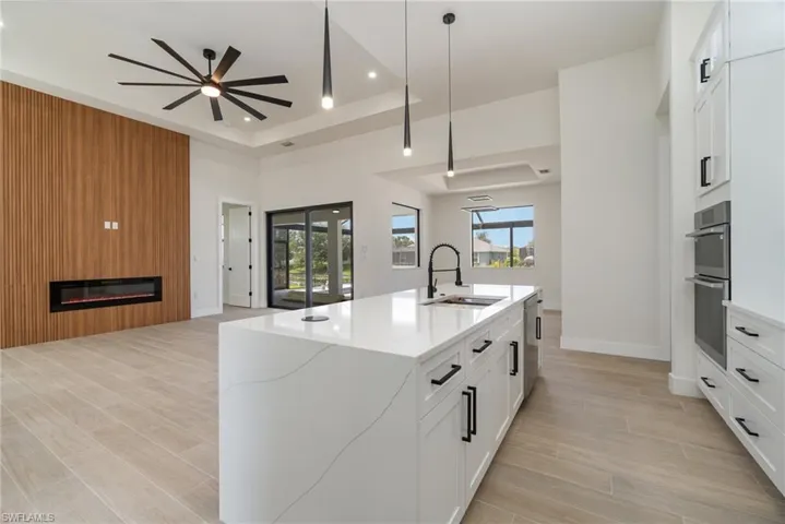 Kitchen with a raised ceiling, a fireplace, pendant lighting, white cabinetry, and ceiling fan