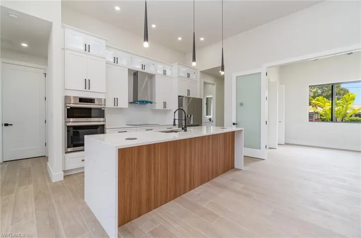 Kitchen featuring stainless steel appliances, a kitchen island with sink, white cabinets, sink, and wall chimney exhaust hood