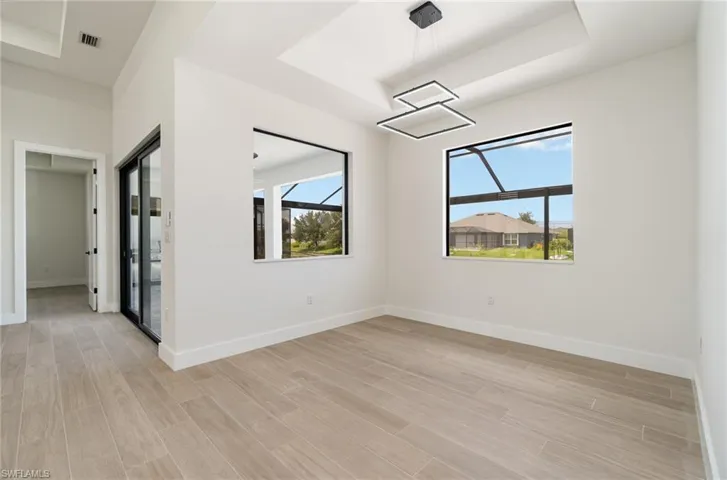 Empty room with light wood-type flooring, a raised ceiling, and a healthy amount of sunlight