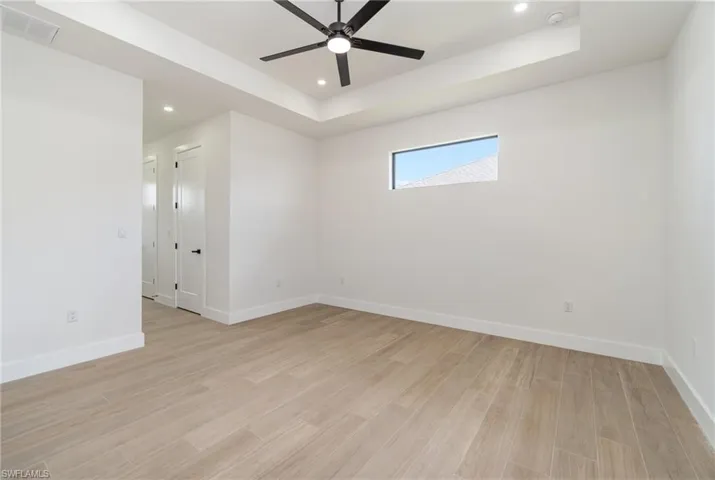 Unfurnished room with light hardwood / wood-style flooring, a tray ceiling, and ceiling fan