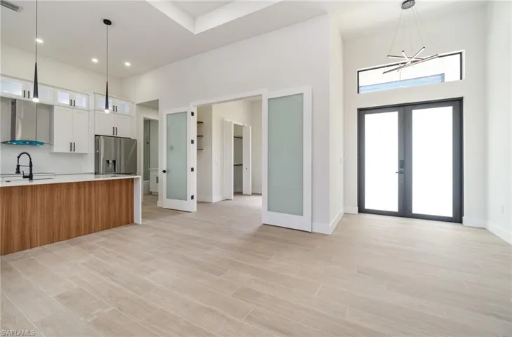 Kitchen featuring french doors, white cabinets, decorative backsplash, wall chimney exhaust hood, and stainless steel refrigerator with ice dispenser