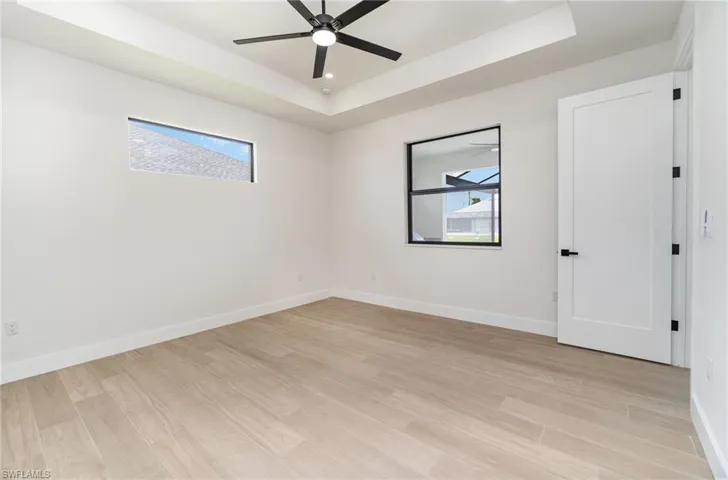 Empty room featuring ceiling fan, a raised ceiling, and light hardwood / wood-style floors