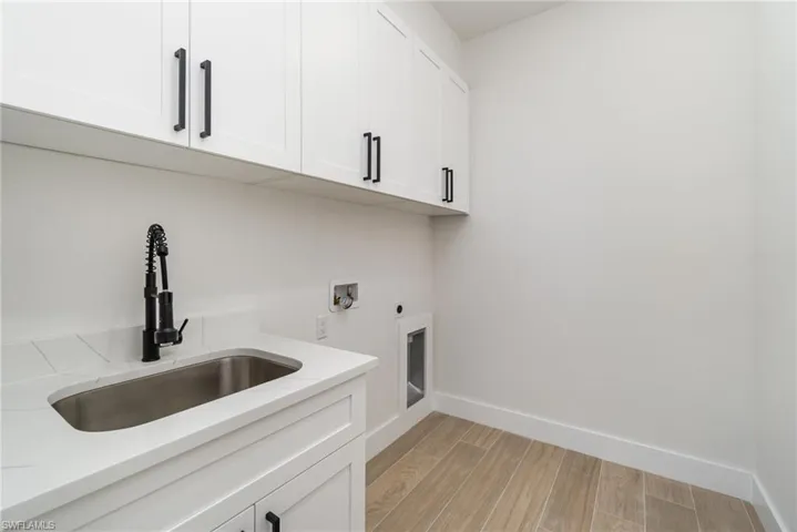 Clothes washing area with cabinets, electric dryer hookup, light hardwood / wood-style flooring, sink, and washer hookup