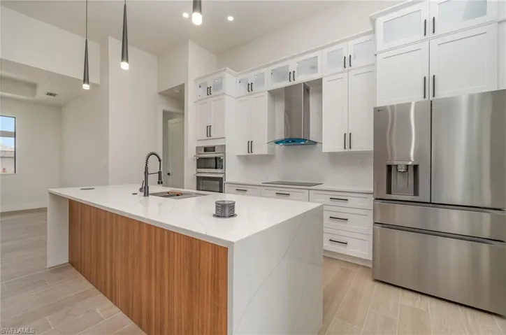 Kitchen with stainless steel appliances, white cabinetry, wall chimney exhaust hood, and decorative backsplash